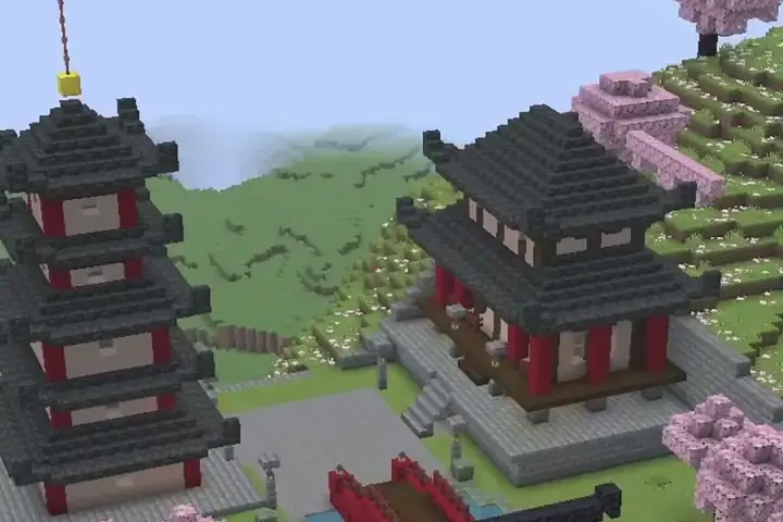 A black and red pagoda and temple hall on a hillside with pink cherry trees